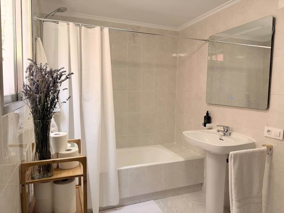 Baño de la Casa A con bañera, cortina blanca, lavabo y espejo con luz