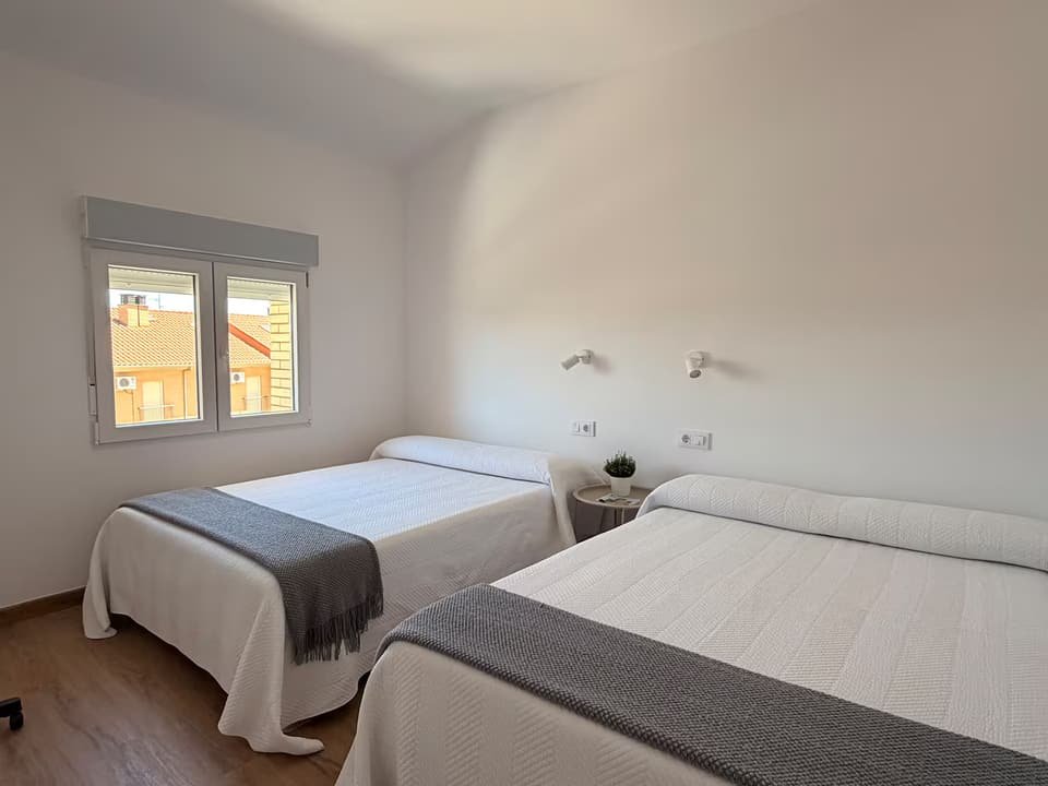 Dormitorio de la Casa A con dos camas, mantas grises y ventana