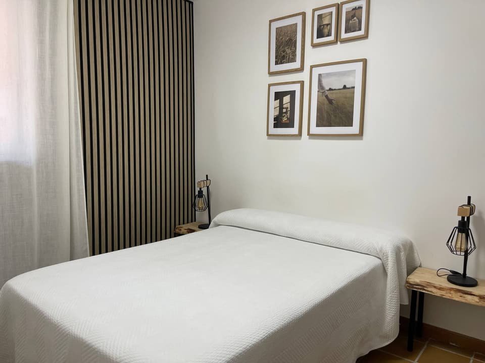 Dormitorio de la Casa B con cama de matrimonio, panel de listones de madera y cuadros